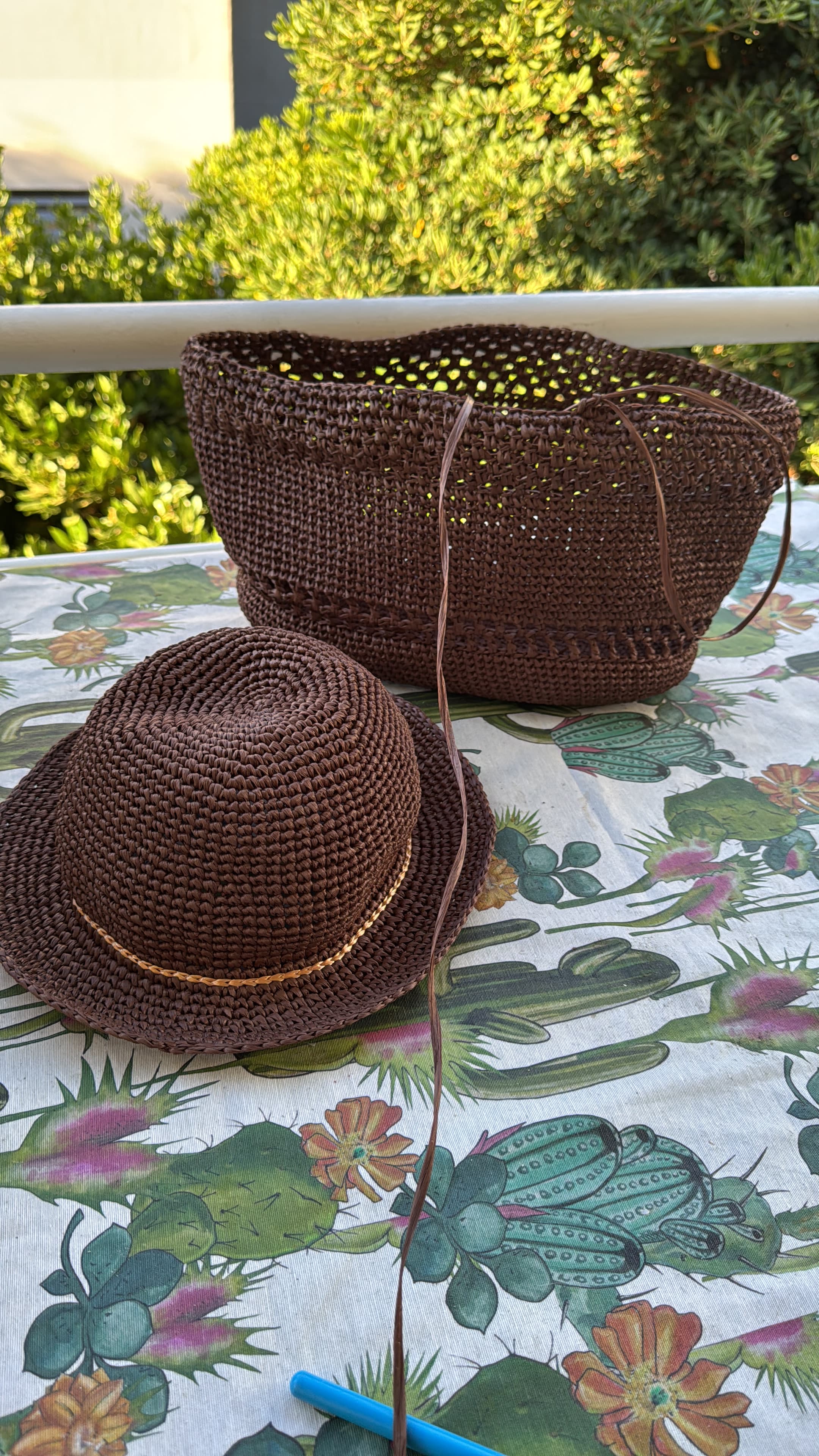 Chapeau et panier en crochet marron sur une nappe à motifs de cactus en extérieur.