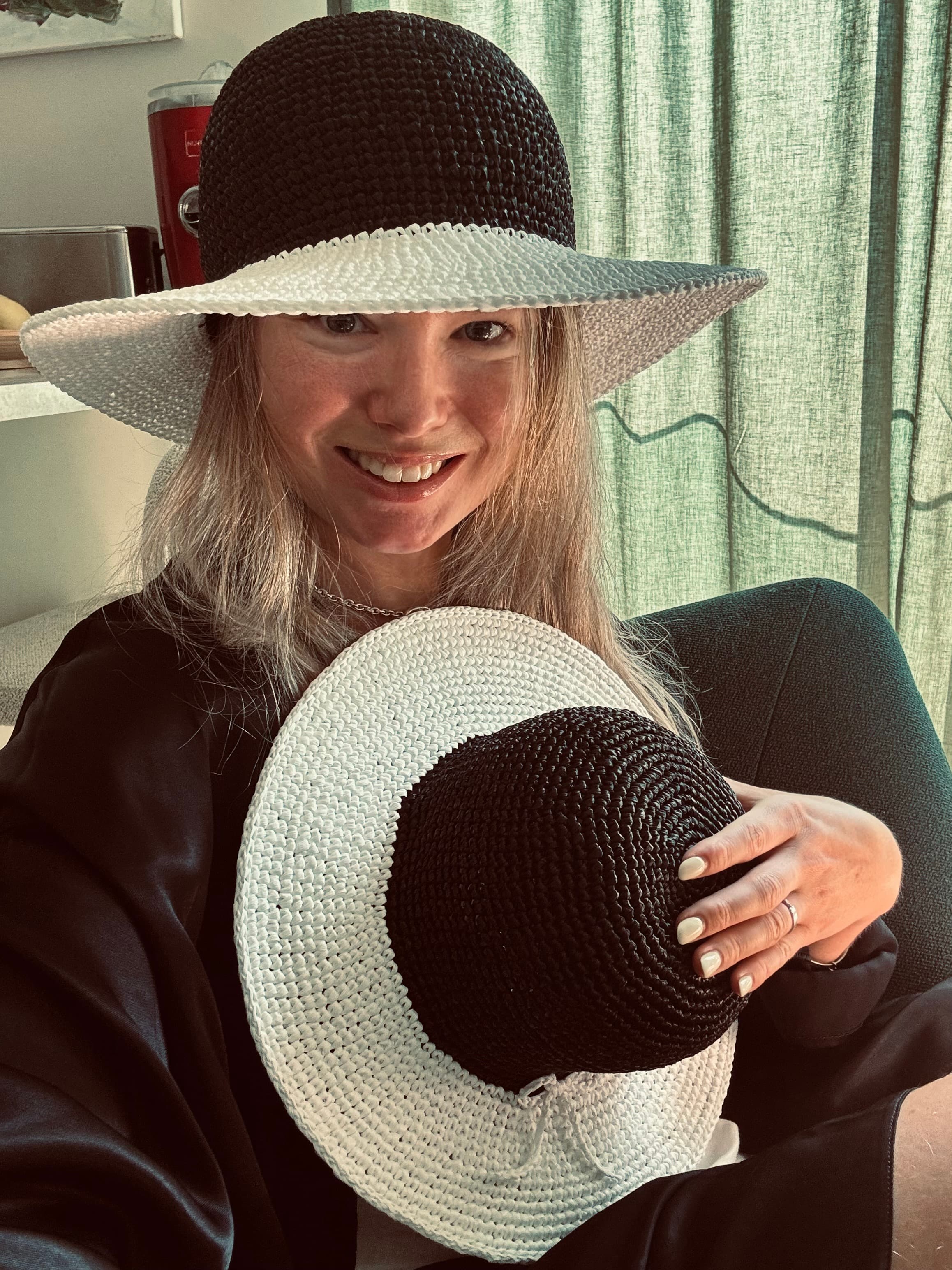 Femme souriante portant un chapeau de paille noir et blanc et tenant un chapeau identique.