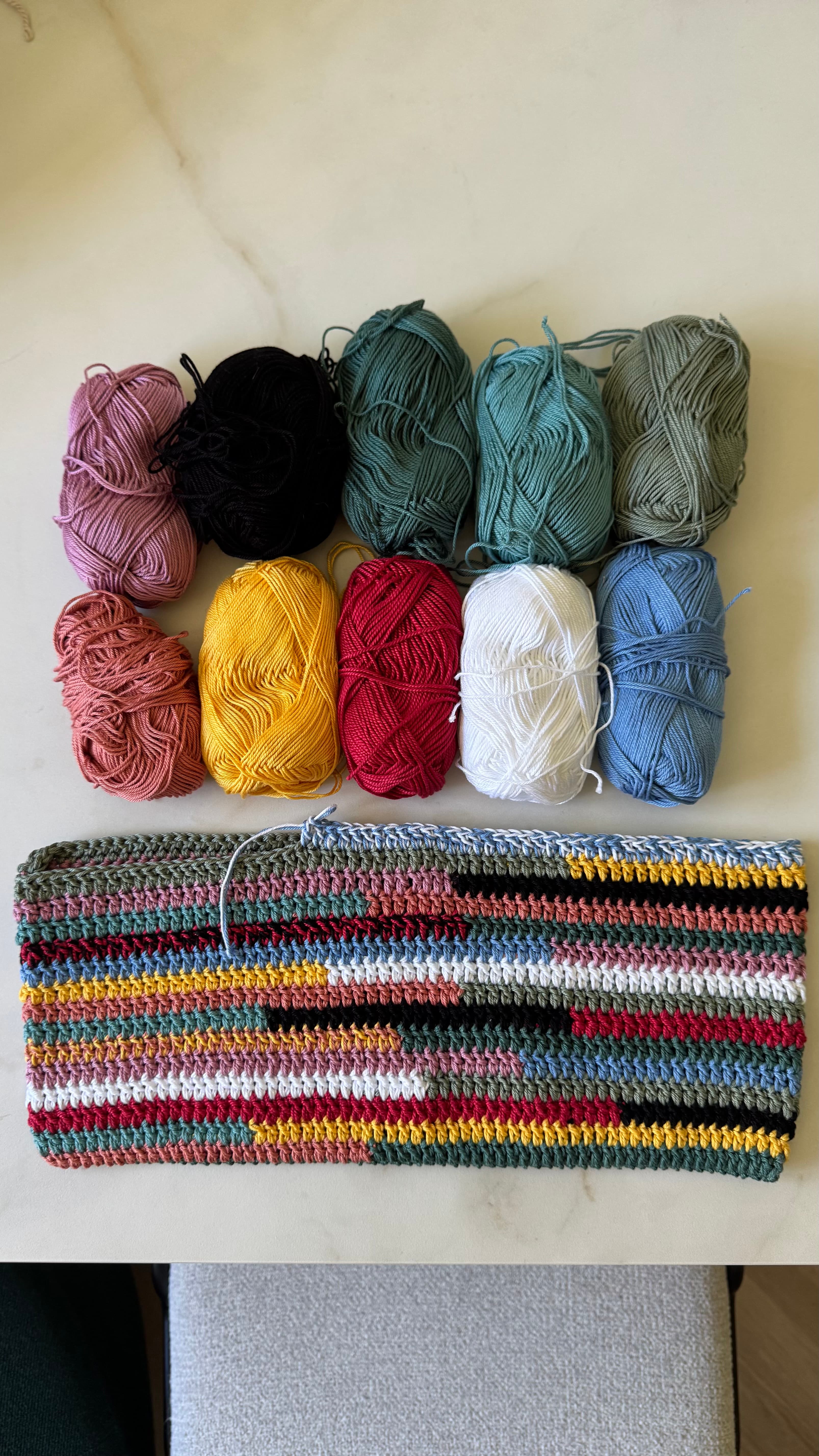Pelotes de laine multicolores disposées au-dessus d'un échantillon de crochet aux rayures horizontales assorties.