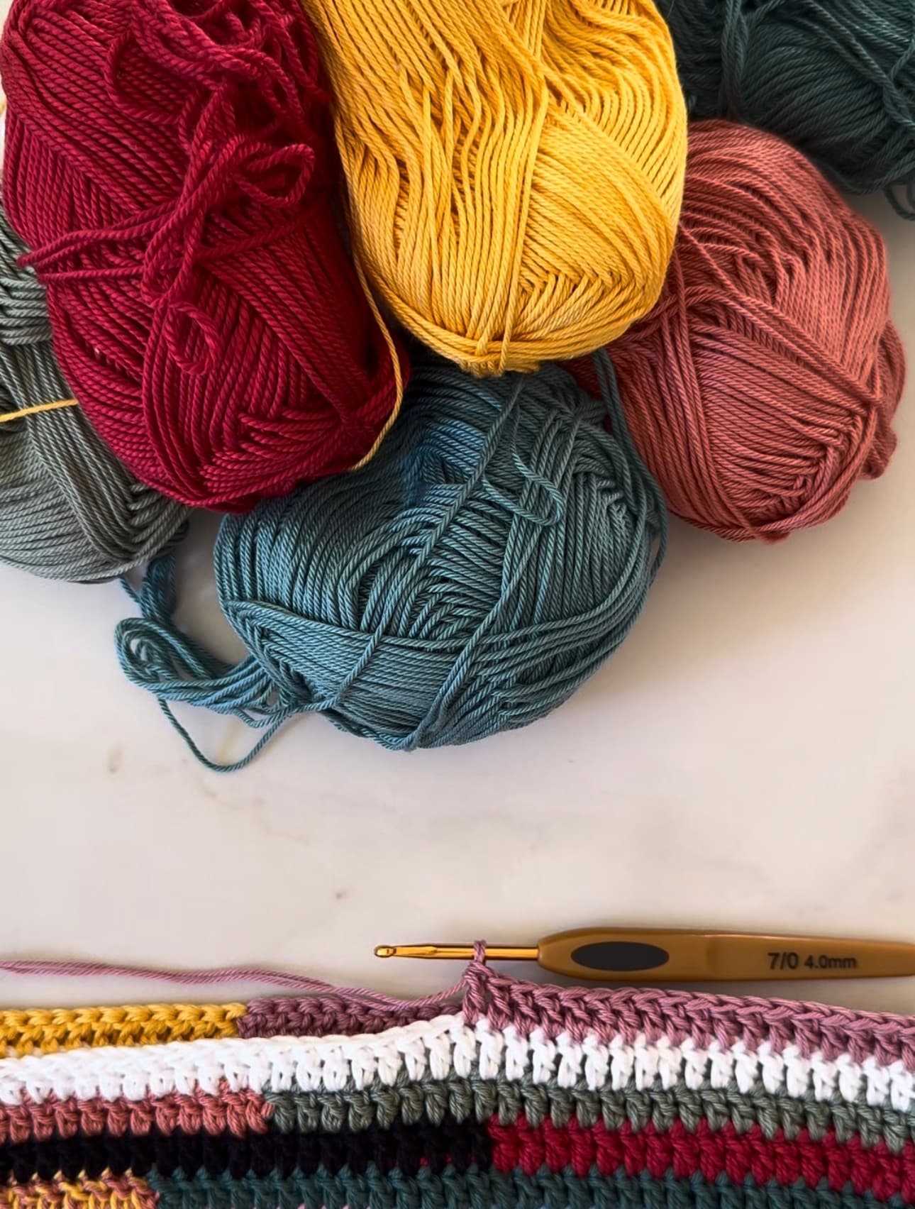 Pelotes de laine colorées et ouvrage au crochet multicolore avec un crochet doré.