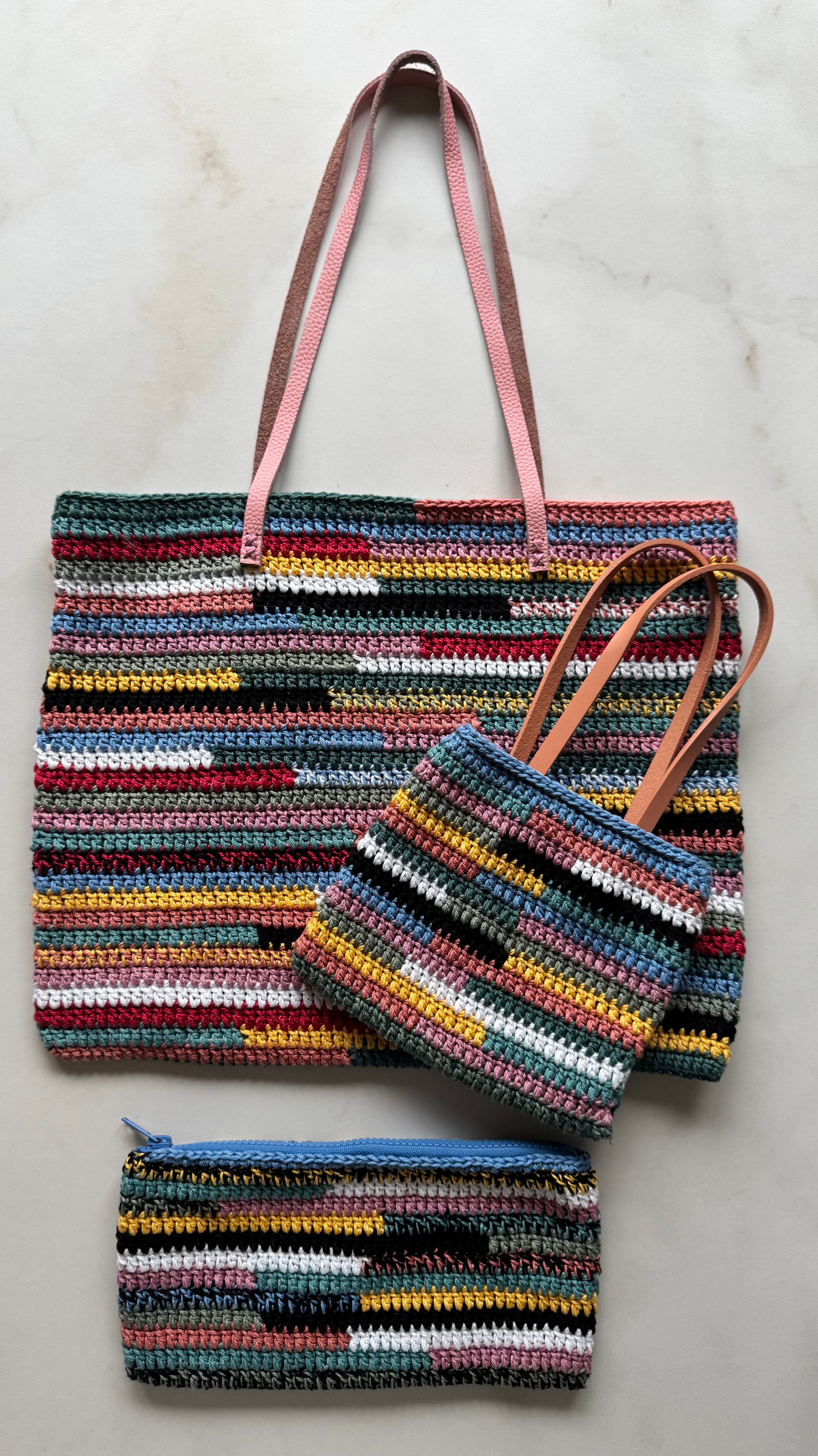 Trois sacs au crochet à rayures multicolores avec des poignées en cuir sur fond clair.