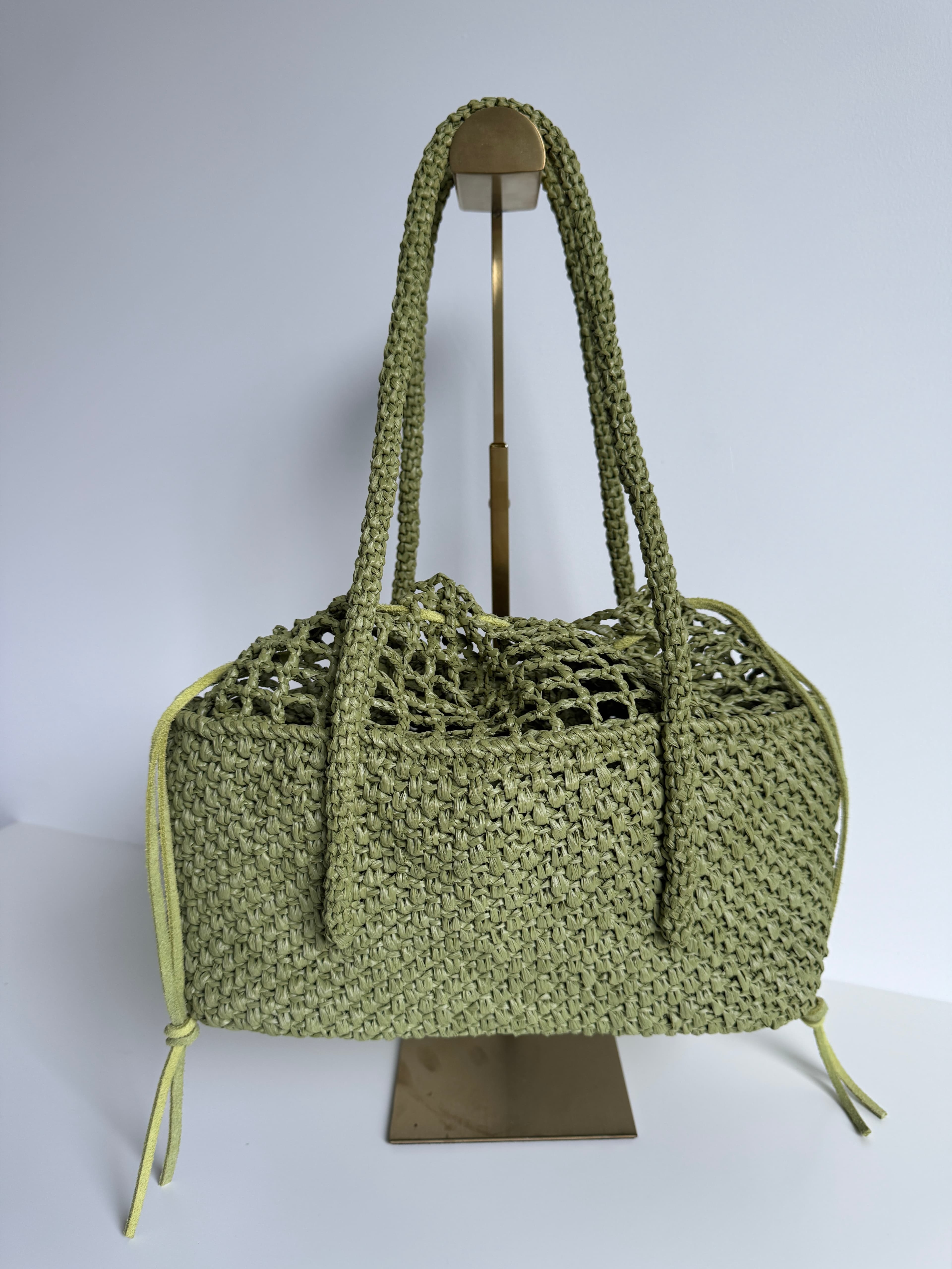 Sac à main tressé vert olive avec longues anses sur un support en métal doré.