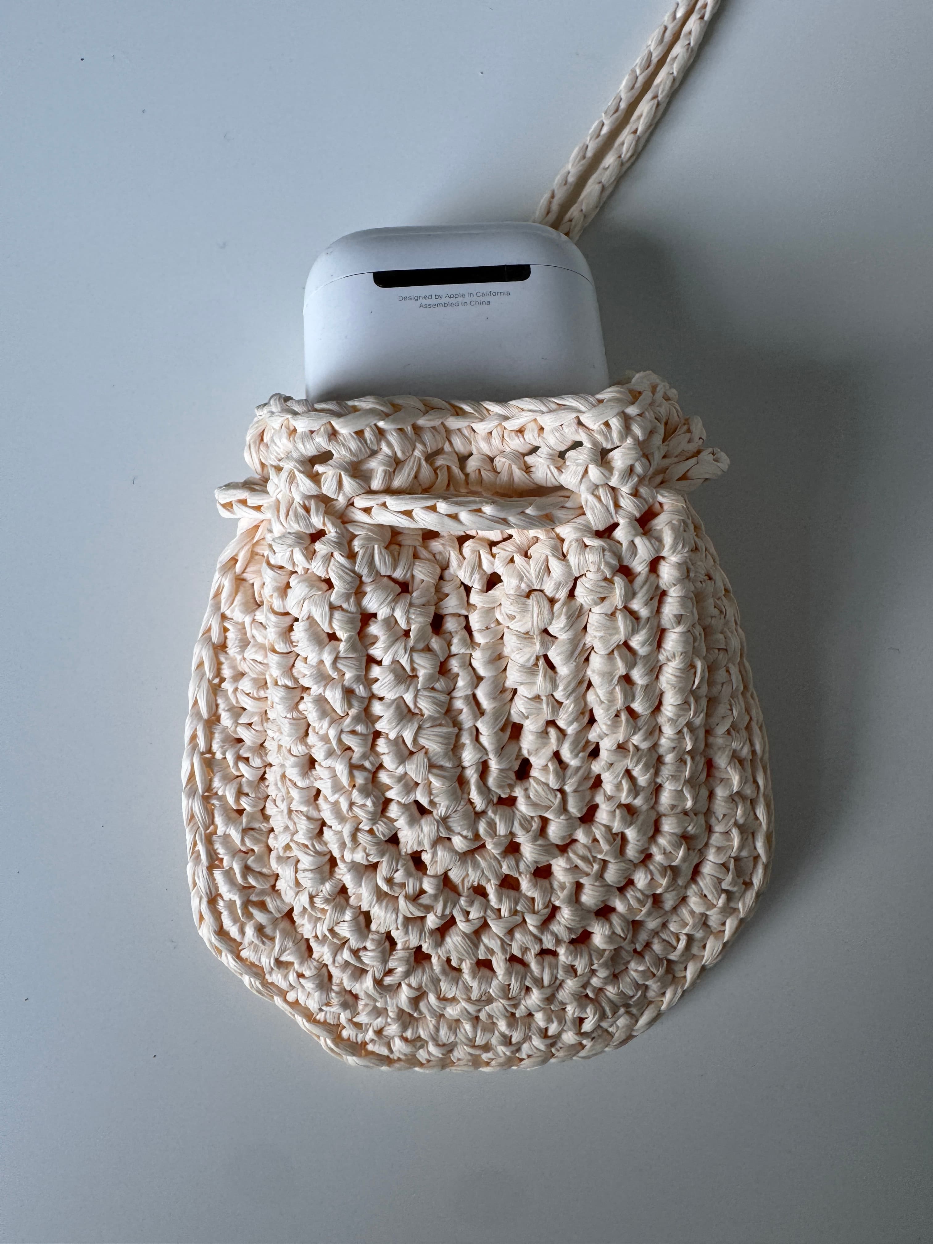 Pochette artisanale en crochet crème avec un étui d'écouteurs blanc sur fond blanc.