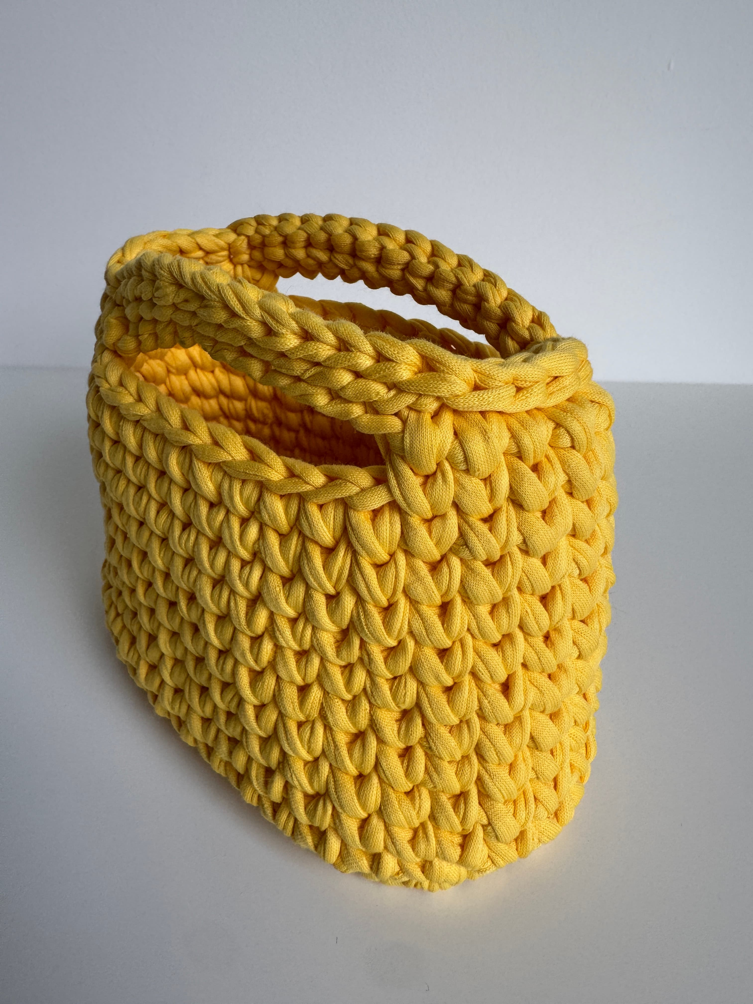 Panier jaune vif crocheté en gros fil de coton avec poignées, sur fond blanc uni.