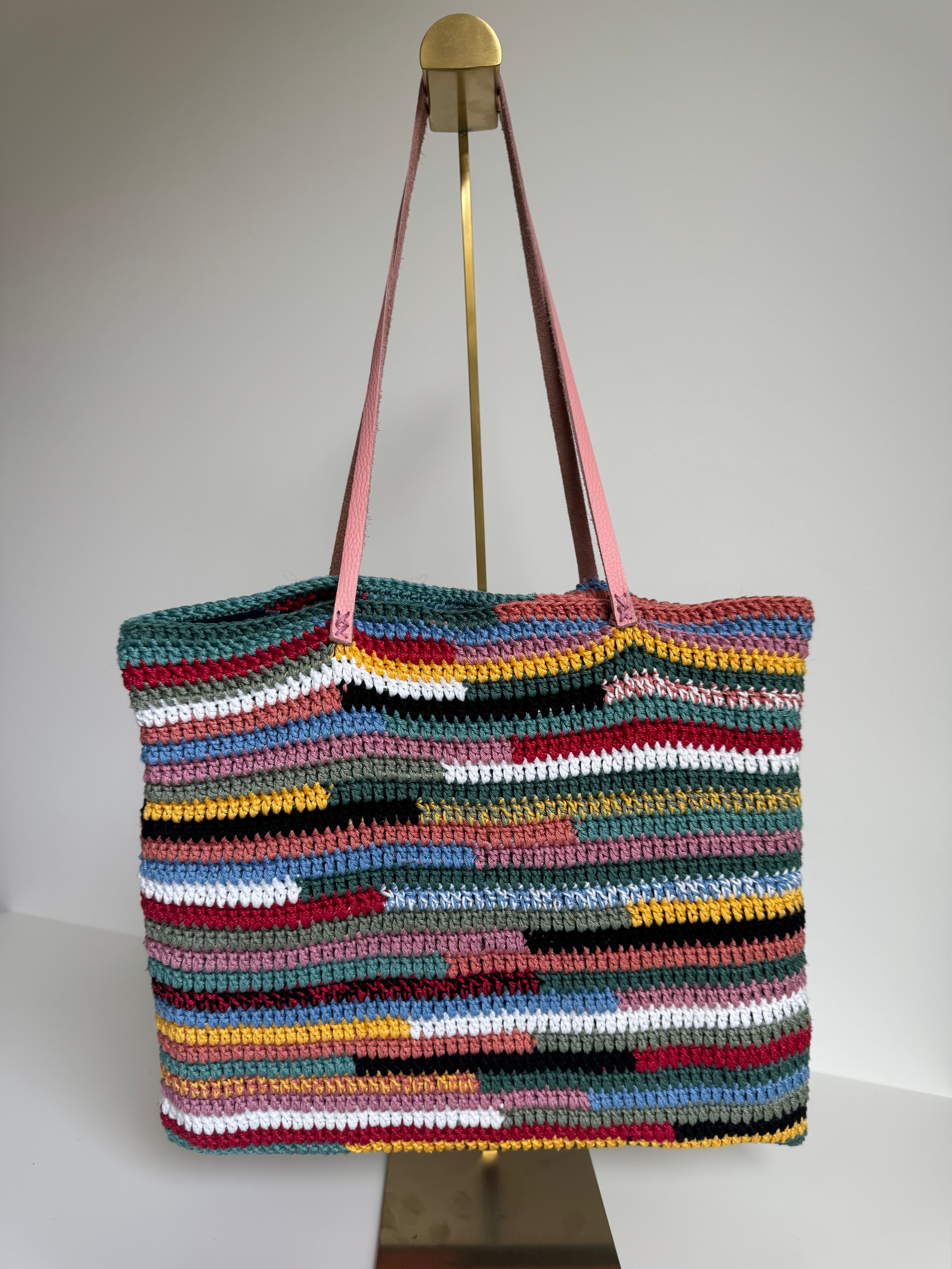 Sac cabas au crochet à rayures multicolores avec de longues anses en cuir rose.