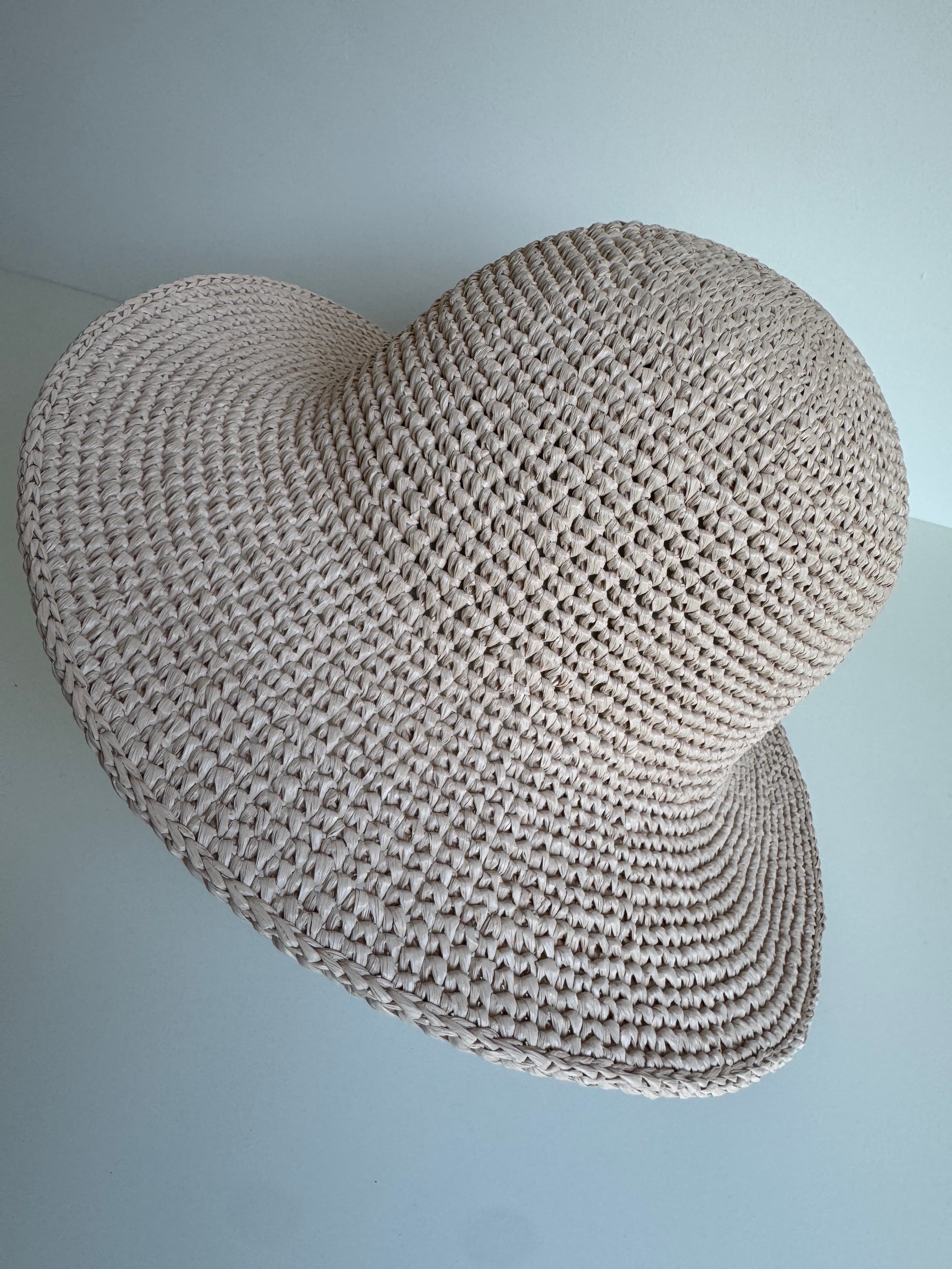 Chapeau de paille beige à larges bords avec un motif tressé sur fond clair.