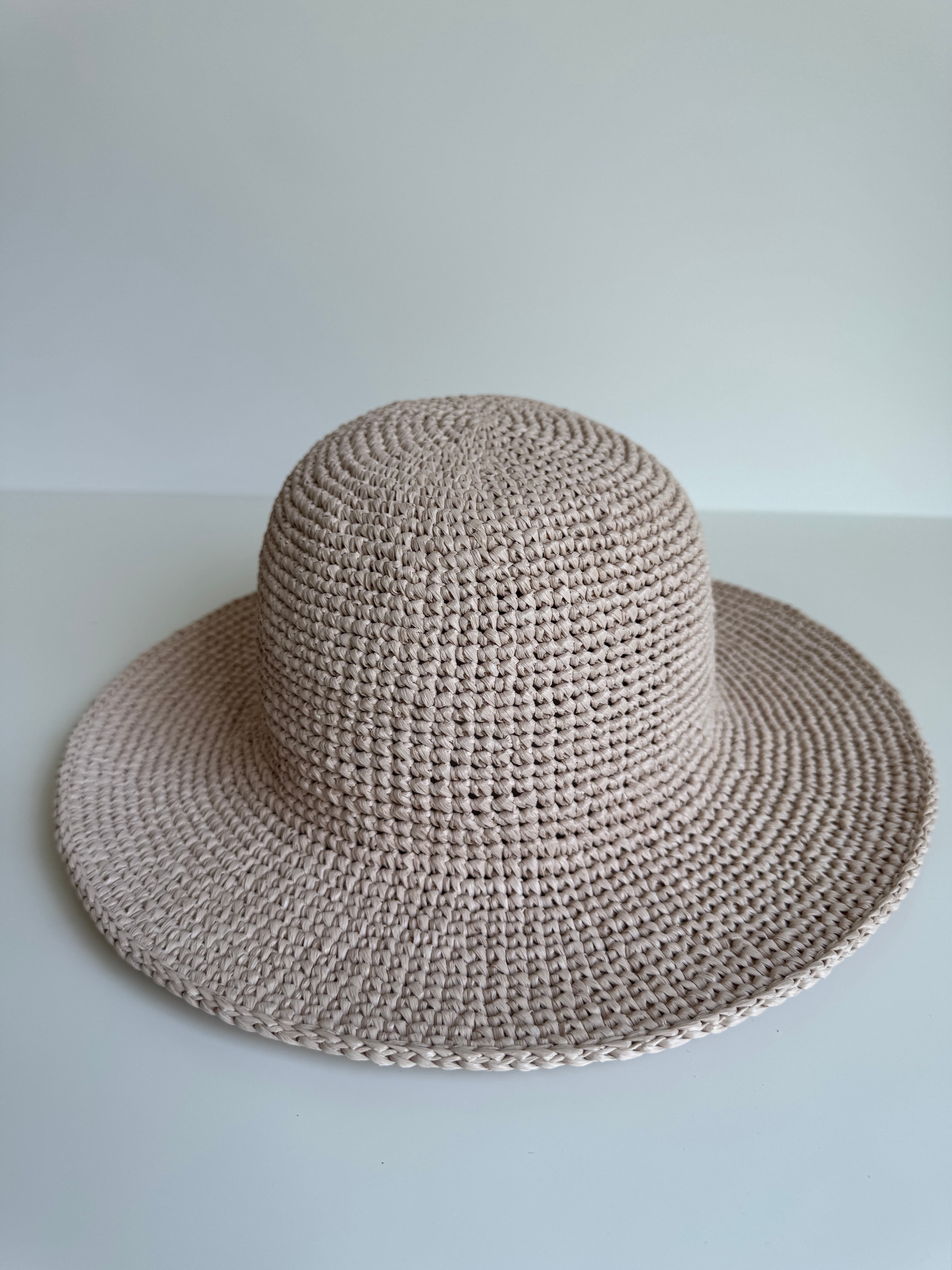 Chapeau de soleil beige crocheté à large bord et calotte arrondie sur une surface blanche.