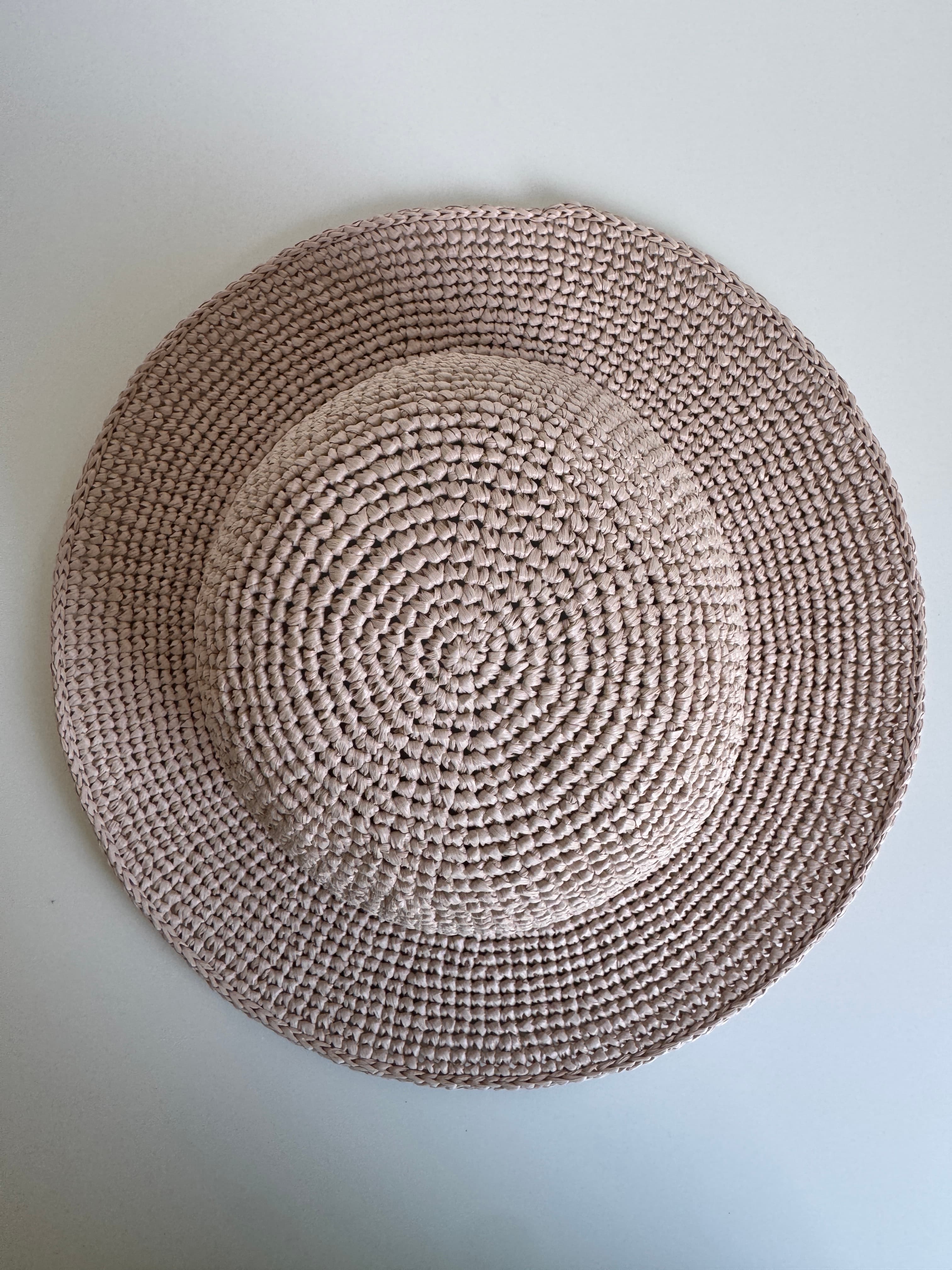 Chapeau de soleil en paille tressée beige rosé, vu de dessus sur fond blanc.