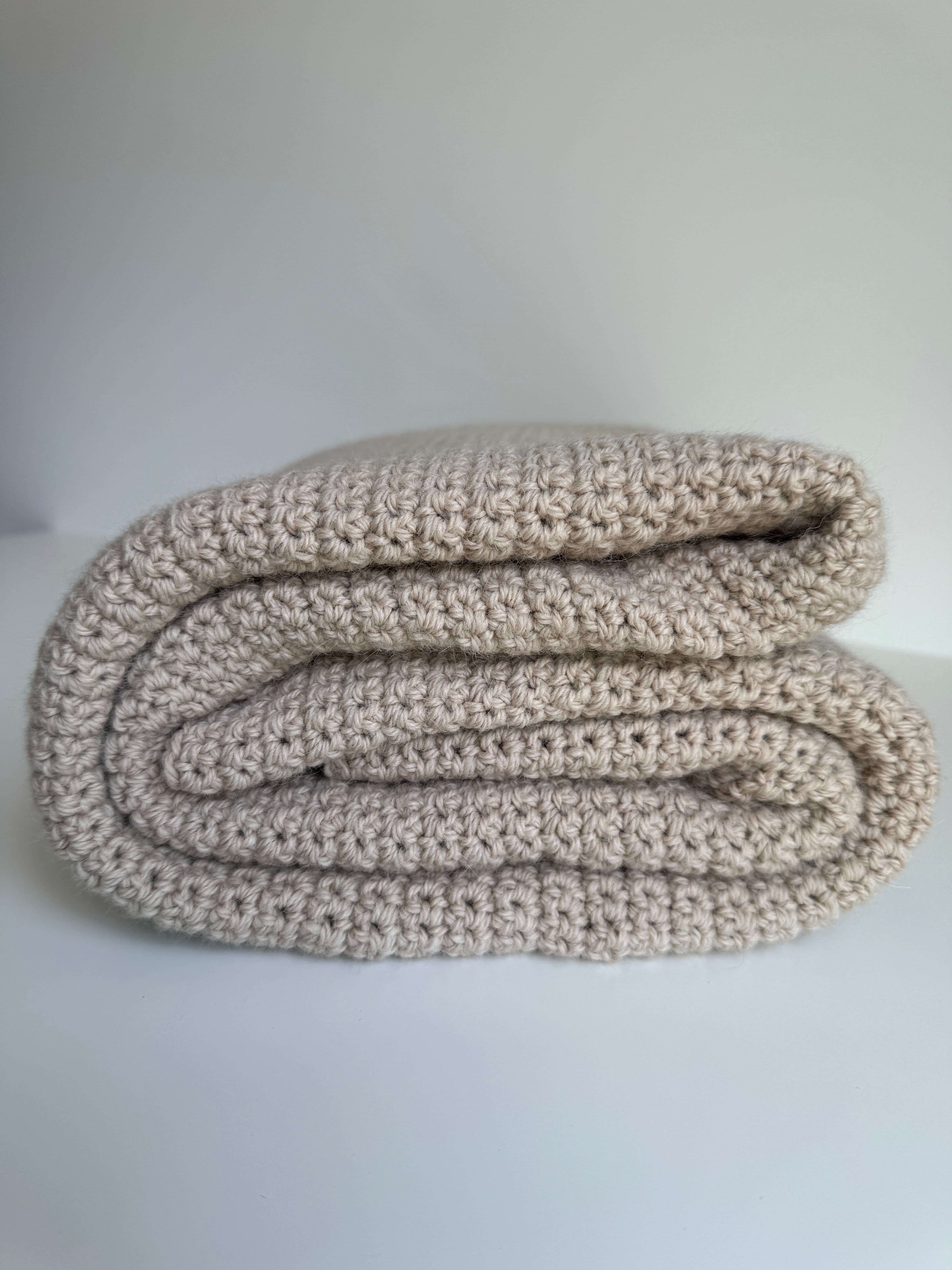 Couverture beige pliée au crochet épais avec une texture de points serrés sur fond blanc.