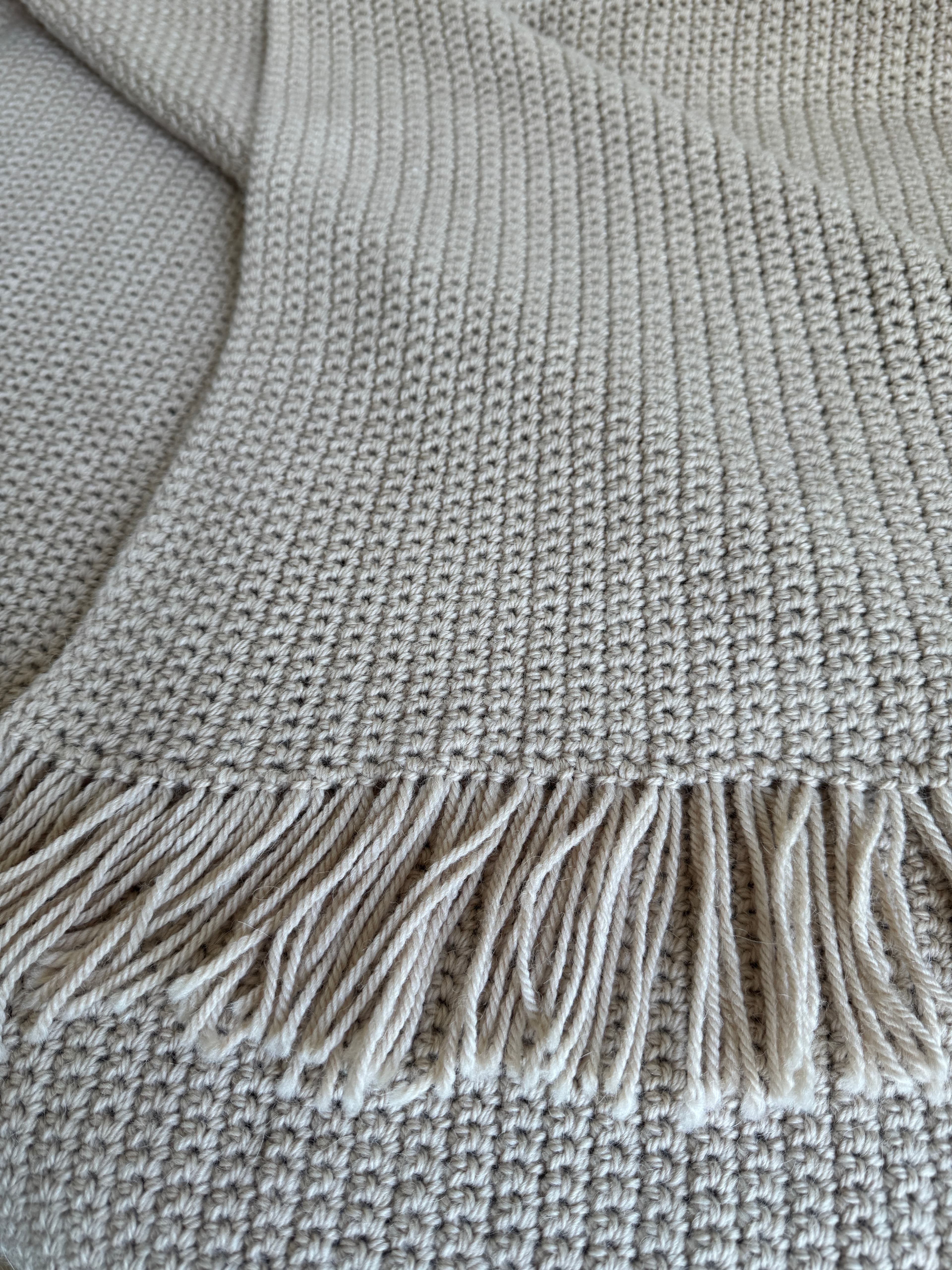 Gros plan d'une couverture en crochet beige avec un point texturé et des franges décoratives.