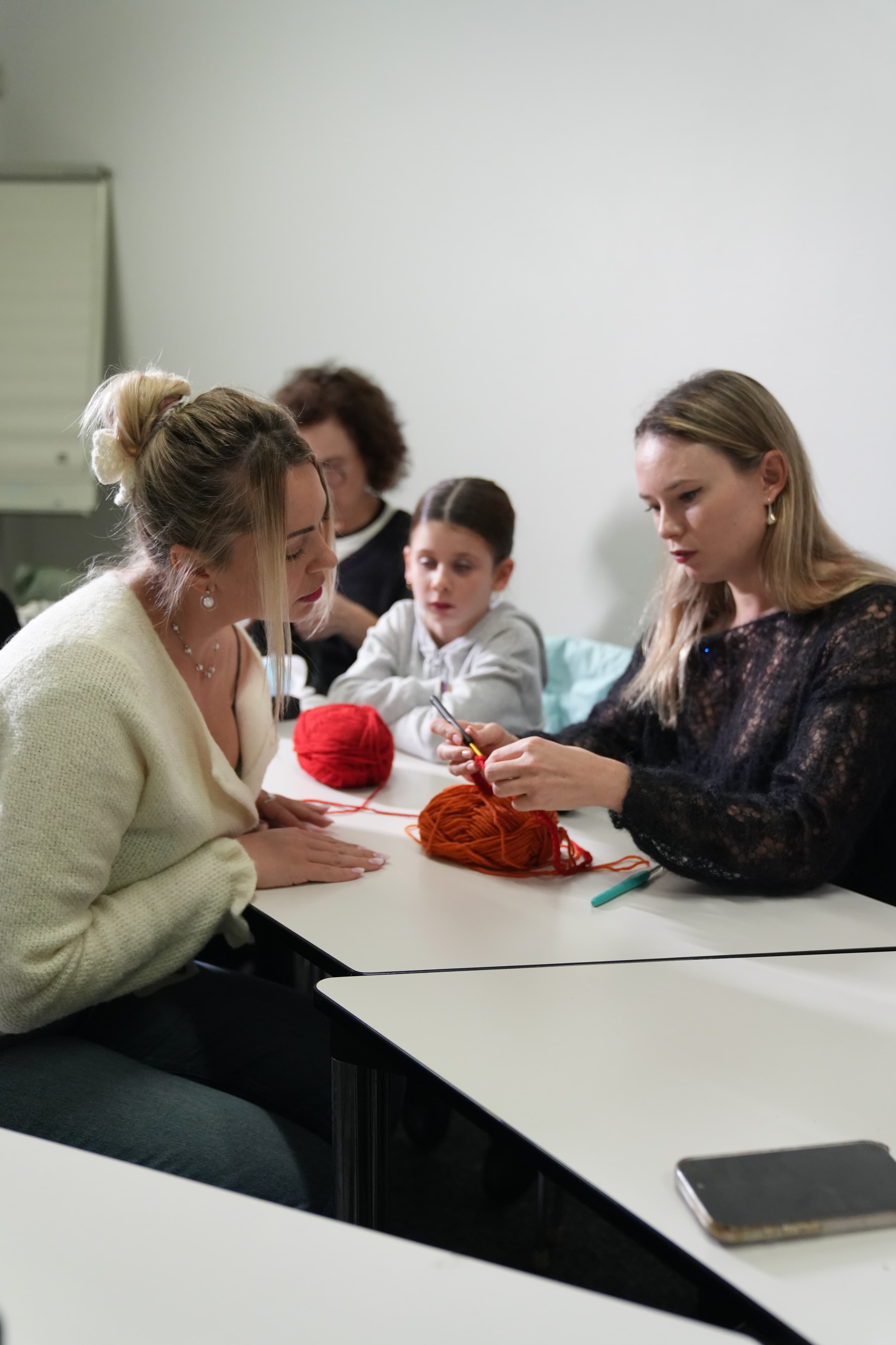 Deux femmes et une enfant pratiquent le crochet avec de la laine orange et rouge.
