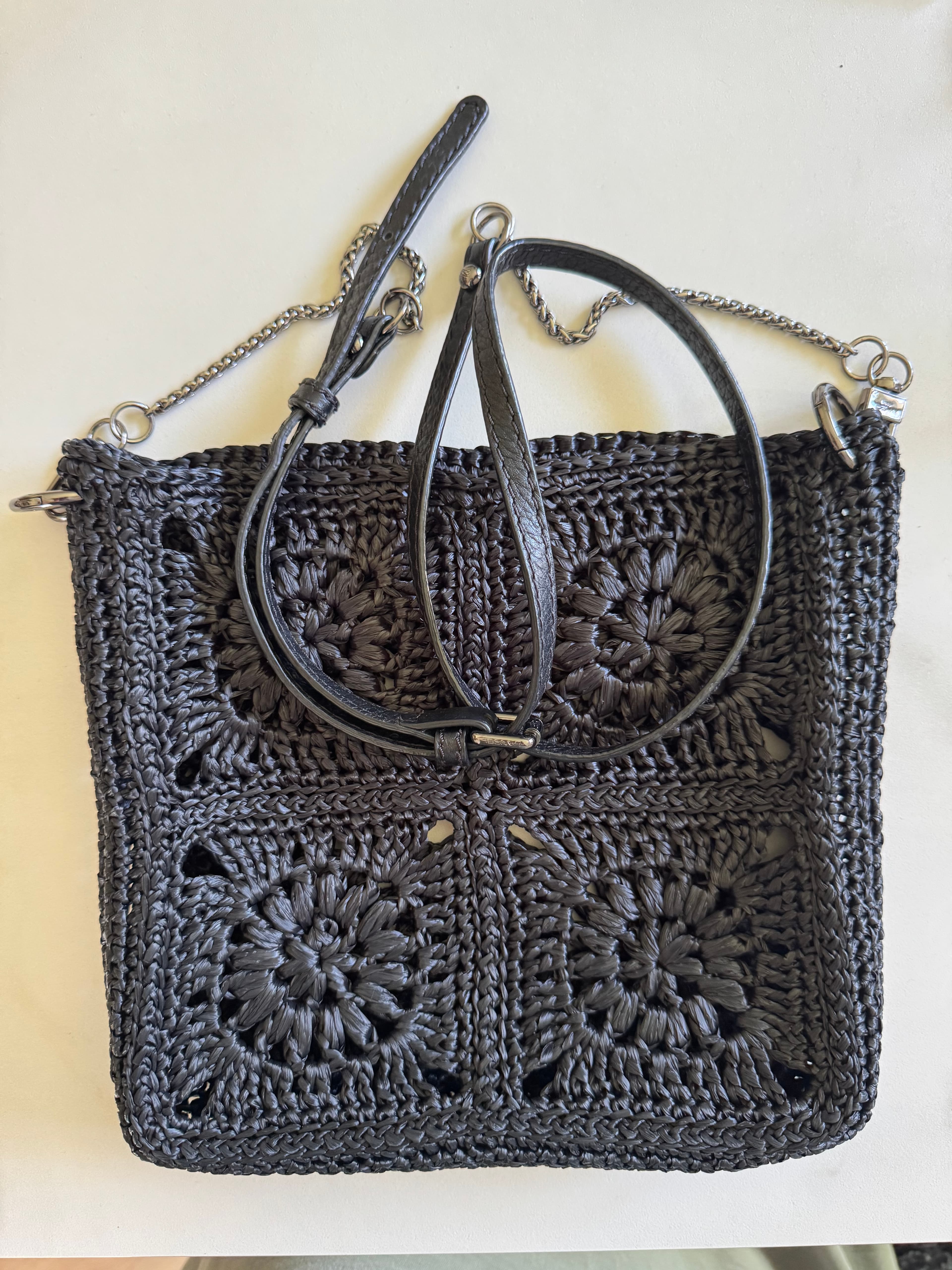Sac à main noir crocheté aux motifs floraux avec bandoulière en cuir et chaîne argentée.